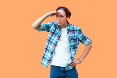 Sıradan mavi kareli gömlek ve saç bandı takmış, alnında el ve turuncu arka planda duran genç, düşünceli, ciddi bir adam..