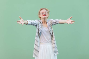 açık yeşil arka plan üzerinde sarılma jest gösterirken gülümseyerek ve gözlük ile beyaz çizgili bluz mutlu genç sarışın kadın