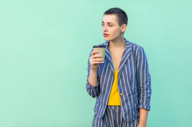 sarı gömlek ve çizgili takım elbise li kısa saç güzel hipster kadın dinlenme kahve içme ve yeşil arka plan üzerinde uzağa bakıyor