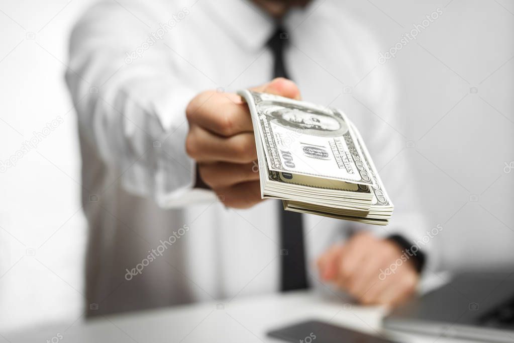 richman investor in white shirt and black tie sitting in office and giving money on grey background