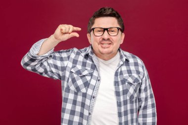 damalı gömlek ve gözlük umutlu yakışıklı orta yaşlı adam kameraya bakarak ve koyu kırmızı arka plan üzerinde daha fazla bir şey isteyen.
