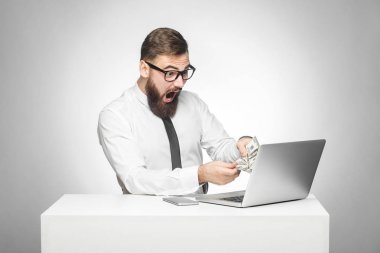  beyaz gömlek sürpriz yüz ile nakit tutarak duygusal şok işadamı ve ağız açtı ve gri arka planda laptop bakıyor. ofiste oturan 