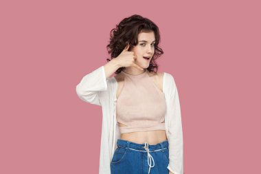 komik güzel esmer genç kadın rahat tarzı kıvırcık saç modeli ile arama el hareketi ile ayakta ve pembe arka plan üzerinde kamera bakarak