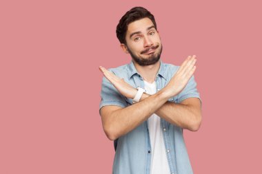 ciddi yakışıklı sakallı genç adam mavi rahat tarzı gömlek X işareti elleri ile ayakta ve pembe arka plan üzerinde kamera bakarak