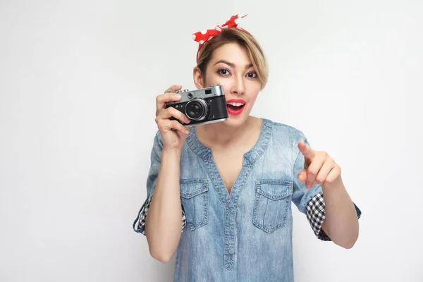 若いですブロガー女の子でカジュアルデニムシャツとともに化粧と赤ヘッドバンド保持レトロカメラと指差し指でカメラ隔離された上の白の背景 — ストック写真