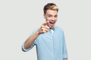 açık mavi gömlek gösteren ve gri arka planda sürpriz mutluluk yüzü ile kameraya bakarak hayran yakışıklı genç adam