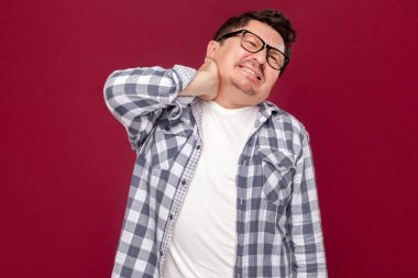 rahat damalı gömlek ve gözlük onun ağrılı boyun tutan ve koyu kırmızı arka plan üzerinde dişleri sıkma orta yaşlı işadamı