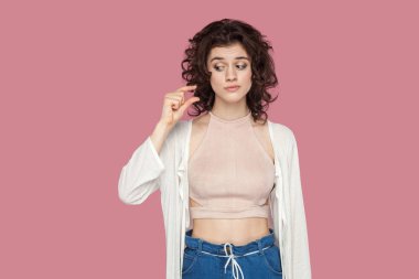rahat tarzı ayakta kıvırcık saç modeli ile güzel esmer genç kadın ayakta ve pembe arka plan üzerinde parmakları ile biraz jest gösteren