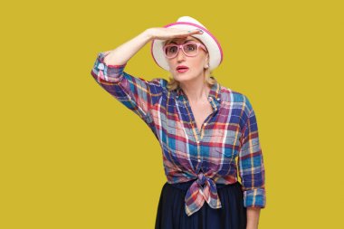 sarı arka planda alnına el ile duran şapka ve gözlük ile rahat tarzı özenli modern şık olgun kadın