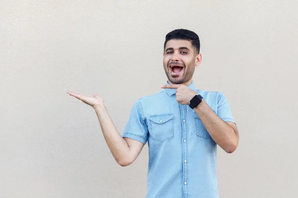 Terkejut Pemuda Tampan Berjenggot Dengan Kemeja Biru Menunjuk Tangan Kosong — Stok Foto