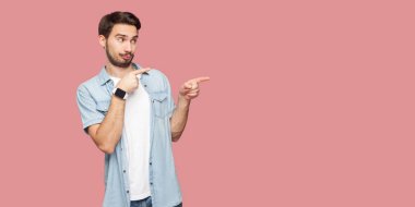 mavi rahat tarzı gömlek özenli yakışıklı sakallı genç adam görünümlü ve pembe arka plan üzerinde bir kenara işaret