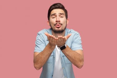 mavi rahat tarzı gömlek aşık yakışıklı sakallı genç adam mutlu kamera bakıyor ve pembe arka plan üzerinde hava öpücük gönderme