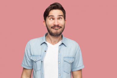 mavi rahat tarzı gömlek deli yakışıklı sakallı genç adam çapraz gözleri ile ayakta ve pembe arka plan üzerinde komik komedyen yüzü ile bakıyor