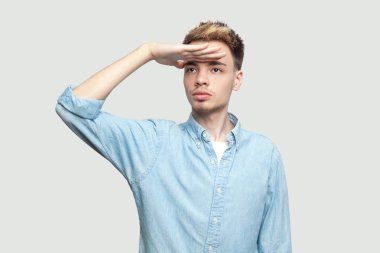 alnında el ile duran ve gri arka plan üzerinde ciddi bir yüz ile uzağa bakarak açık mavi gömlek ciddi özenli yakışıklı genç adam 
