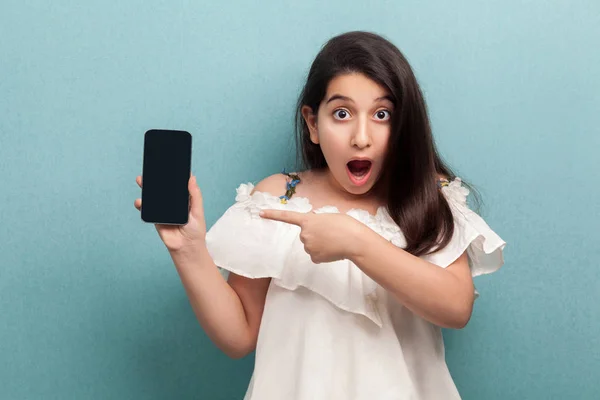 Impactado Hermosa Adolescente Vestido Blanco Sosteniendo Teléfono Inteligente Señalando Dedo — Foto de Stock