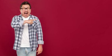 şok yüz ve koyu kırmızı arka planda kenara işaret kamera bakarak damalı gömlek ve gözlük hayran yakışıklı orta yaşlı adam