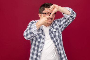 dikkatli yakışıklı orta yaşlı işadamı rahat damalı gömlek ve gözlük kırpma elleri kompozisyon gösteren ve koyu kırmızı arka plan üzerinde hedef bakarak