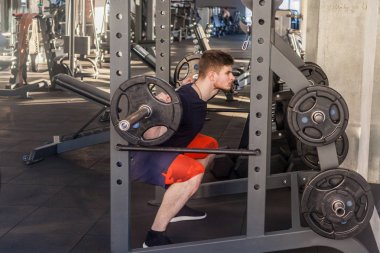 Spor salonunda genç yetişkin vücut geliştirmeci egzersiz yan görünümü ve barbell kaldırma hazırlanıyor, bacaklar için egzersizler yapıyor, sağlıklı yaşam tarzı kavramı