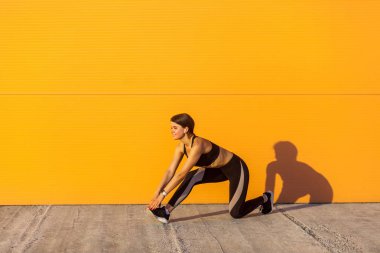 Turuncu duvar arka plan, spor ve sağlıklı bir kavram karşısında diz üzerinde dururken siyah spor giyim genç güzel sportif yogi kadın yan görünümü