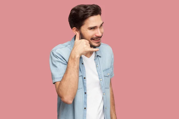 快乐英俊的胡子年轻人在蓝色休闲衬衫显示呼叫手势手在耳朵上 看着粉红色的背景相机 — 图库照片