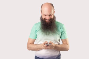 mutlu orta yaşlı kel sakallı adam akıllı telefon ekranına bakıyor ve gri arka planda dişli gülümseme ile mesaj okuma.