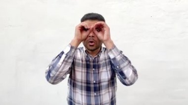 mavi damalı gömlek şok yakışıklı sakallı adam gözlerde dürbün jest elleri gösteren ve beyaz duvar arka planda şaşkın yüz ile etrafa bakıyor