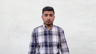 mavi damalı gömlek üzgün yakışıklı sakallı adam kulaklarıparmak koyarak ve beyaz duvar arka plan üzerinde tatminsiz yüzü ile kamera bakıyor