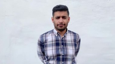 mavi damalı gömlek komik yakışıklı sakallı adam eğlenceli yüzü ile kameraya bakıyor ve beyaz duvar arka plan üzerinde gözlerini ve kaşlarını hareket