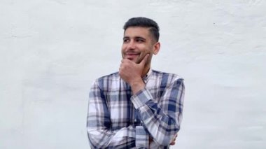 mavi damalı gömlek rüya gibi yakışıklı sakallı adam çenesini dokunmadan ve beyaz duvar arka planda dişli gülümseme ile rüya görürken uzağa bakıyor