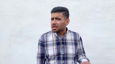 ciddi yakışıklı sakallı adam mavi damalı gömlek kulak el tutan ve beyaz duvar arka planda kamera dikkatli bakıyor