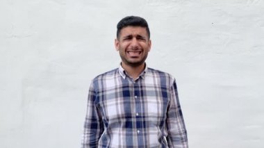 beyaz duvar arka plan etrafında bakarken çapraz parmakları ve sıkma dişleri gösteren mavi damalı gömlek umutlu yakışıklı sakallı adam