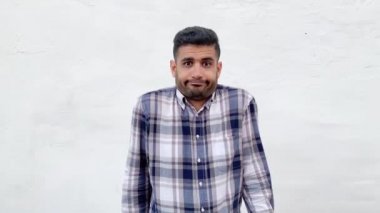 mavi damalı gömlek karışık yakışıklı sakallı adam kaldırdı kolları ile ayakta ve beyaz duvar arka planda karışık yüzü ile kamera bakıyor