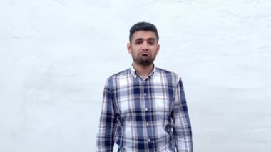 emin memnun yakışıklı sakallı adam mavi damalı gömlek Ok işareti jest gösteren ve beyaz duvar arka planda kamera bakarak