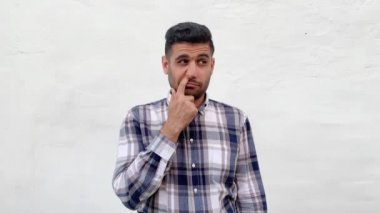 mavi damalı gömlek deli kirli yakışıklı sakallı adam komik yüzü ile burnunu delme ve beyaz duvar arka planda dil gösterirken kameraya bakarak