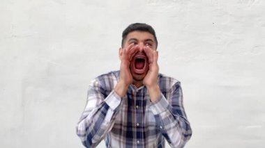 mavi damalı gömlek yakışıklı sakallı adam yüzünde elleri ile ayakta ve beyaz duvar arka plan etrafında çığlık