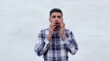 mavi damalı gömlek şok yakışıklı sakallı adam elleri ile yüz dokunmadan ve beyaz duvar arka planda büyük gözlü kamera bakıyor