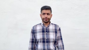 beyaz duvar arka planda şaşkınlık yüz ile düşünürken başını çizerek ve uzağa bakarak mavi damalı gömlek karışık yakışıklı sakallı adam