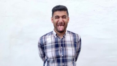 mavi damalı gömlek komik deli yakışıklı sakallı adam kapalı gözleri ile ayakta ve beyaz duvar arka plan üzerinde dil gösteren