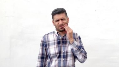 mavi damalı gömlek üzgün hasta yakışıklı sakallı adam yanak dokunmadan ve beyaz duvar arka planda dişleri ağrı hissi
