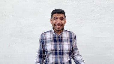 mavi damalı gömlek karışık yakışıklı sakallı adam kaldırdı kolları ile ayakta ve beyaz duvar arka planda karışık yüzü ile kamera bakıyor