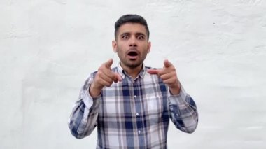 mavi damalı gömlek işaret şok sakallı adam işaret ve beyaz duvar arka plan üzerinde sürpriz inanılmaz mutlu yüz ile kamera bakıyor