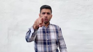 mavi damalı gömlek ciddi sakallı adam işaret ederken suçlayarak ve beyaz duvar arka plan üzerinde kızgın yüzü ile kamera bakıyor