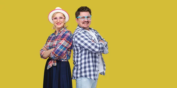 Couple of friends in casual checkered shirts standing together back to back with crossed arms and looking at camera on yellow background