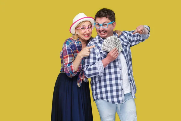 Happy wealthy family in casual checkered shirts standing together and holding fan of dollar money on yellow background