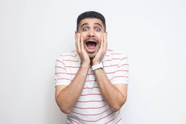 çizgili t-shirt içinde sürpriz yakışıklı sakallı genç adam yüz elleri tutan ve beyaz arka plan izole şaşkın yüzü ile kameraya bakıyor