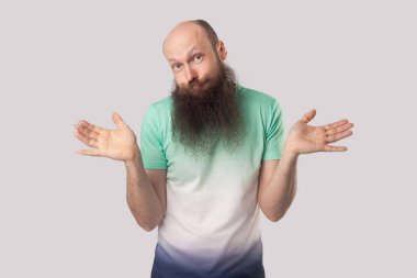 uzun sakallı orta yaşlı kel adam, kolları kaldırıp gri arka planda şüpheli bir yüzle kameraya bakıyor