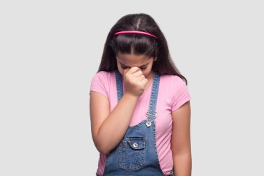 pembe t-shirt ve mavi denim tulum baş aşağı tutarak ve gri arka planda ağlama üzücü güzel esmer kız.