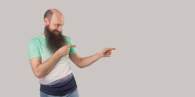 hafif yeşil t-shirt içinde mutlu memnun kel sakallı adamın yan görünümü gri arka planda Toip gülümseme ile bir kenara işaret