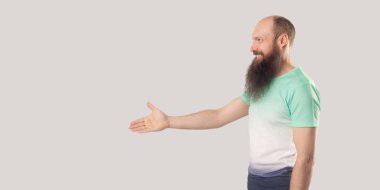 hafif yeşil t-shirt el sıkışması ve gri arka planda Toip gülümseme ile bakarak vererek mutlu memnun kel sakallı adamın yan görünümü