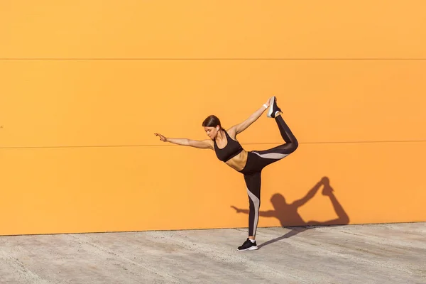 若い魅力的な女性は ヨガを練習し オレンジ色の壁の背景にバランスを保ちながらナタラージャサナ運動に立っています — ストック写真